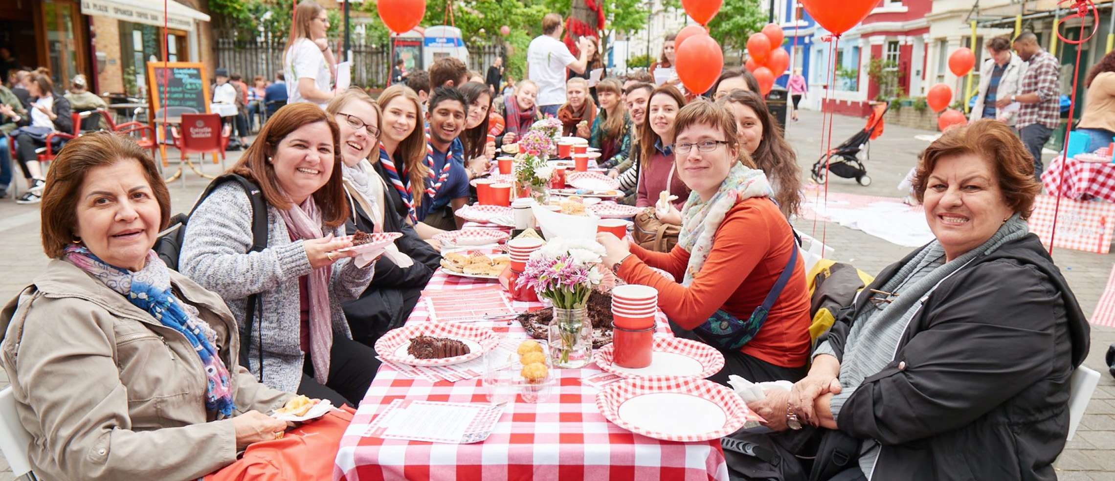 A celebration takes place along a long table, covered in cakes and treats.