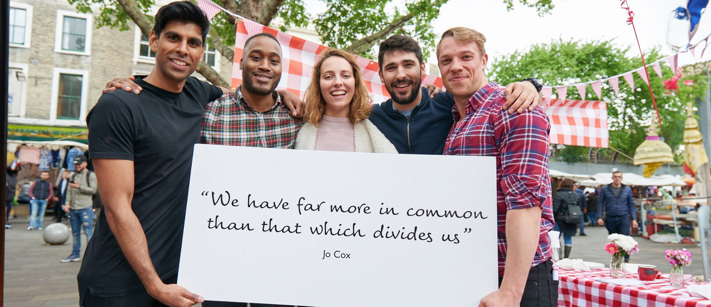 A group of five young people holding up a sign reading "We have far more in common than that which divides us", a quote from Jo Cox.