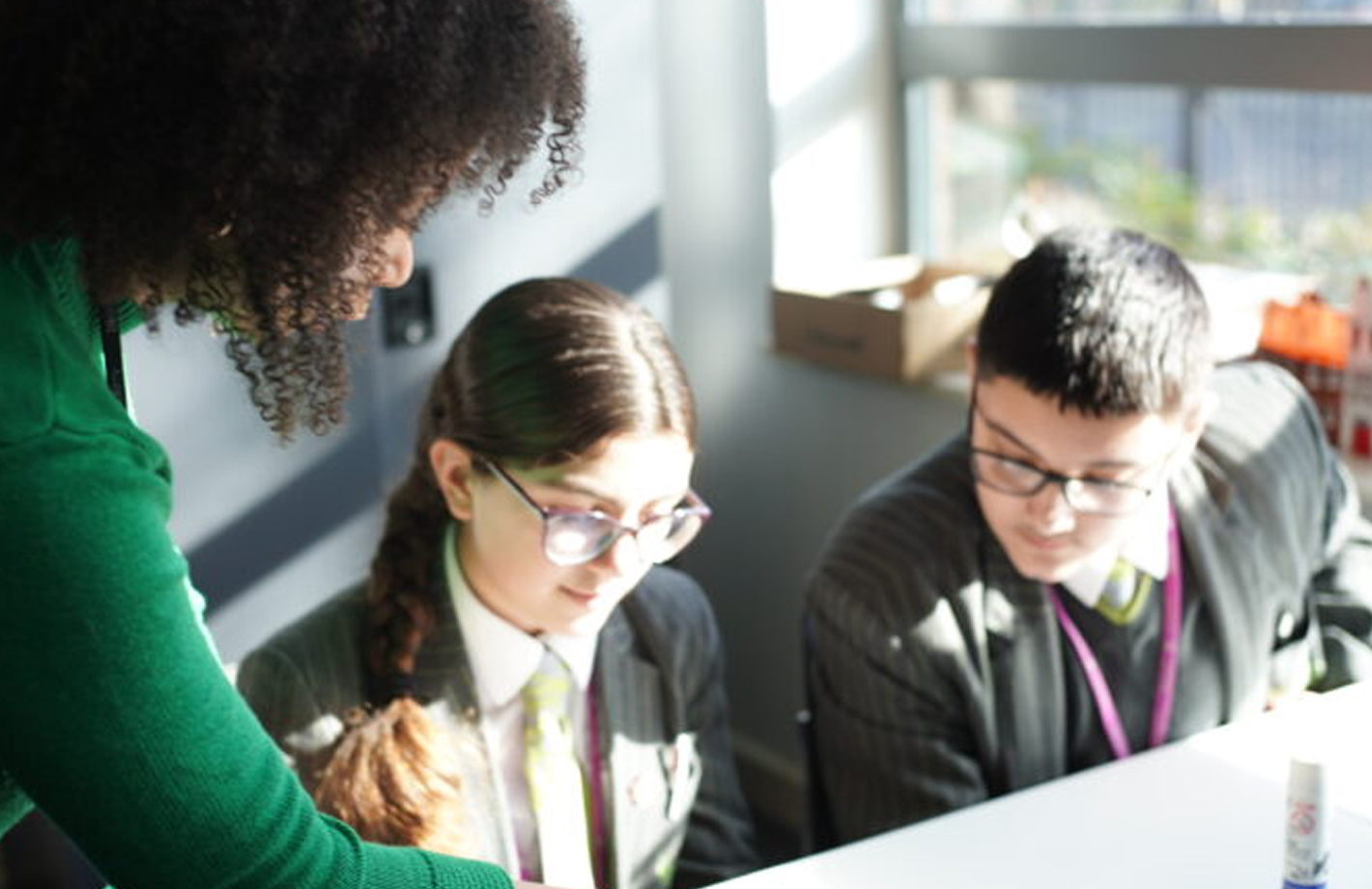 A teacher leans in to support two pupils.