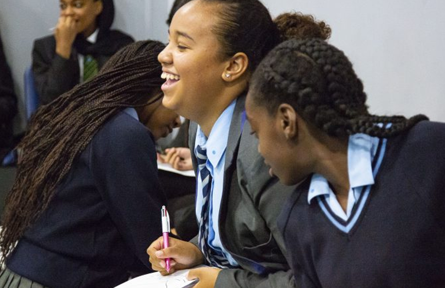 A black school girl laughs whilst sat with her classmates